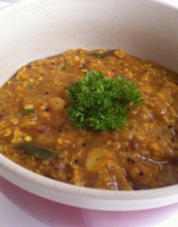 A close up picture of Oats Upma garnished with parsley and served in a white and red bowl.