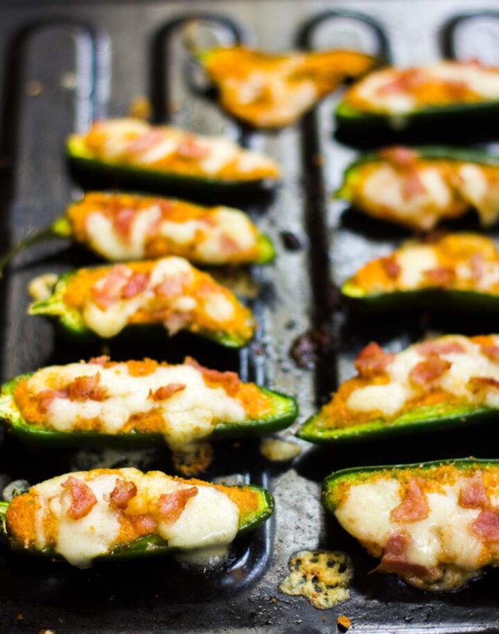 Baked jalapeno poppers lined up on a black tray.