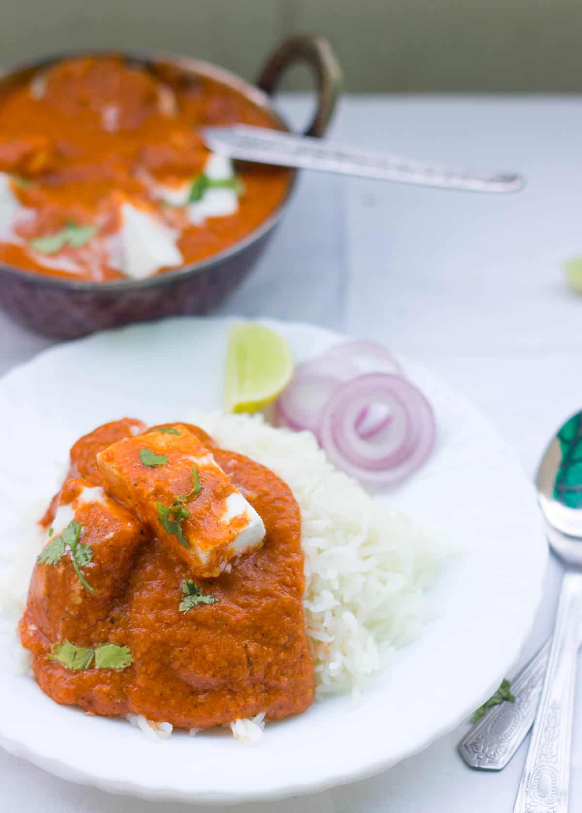 Healthy Paneer Makhani garnished with coriander and served with rice and a side of chopped onions in a white plate.