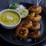 Tandoori Prawns served with mango chutney, onions and lemon in a black plate.