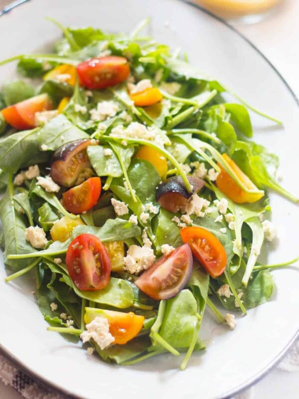 Spinach, Heirloom Tomato and Crumbled Tofu Salad with Roasted Garlic Dressing served in a white plate with extra dressing served on the side.