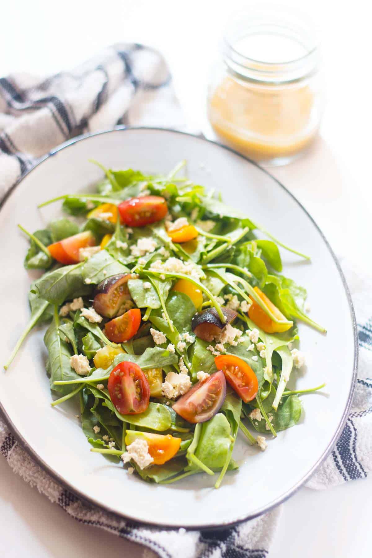 Spinach, Heirloom Tomato and Crumbled Tofu Salad with Roasted Garlic Dressing served in a white plate with extra dressing served on the side.