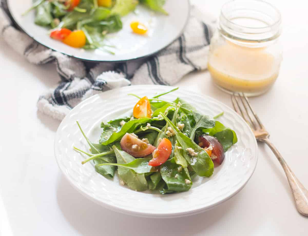 Spinach, Heirloom Tomato and Crumbled Tofu Salad with Roasted Garlic Dressing served in a white bowl.
