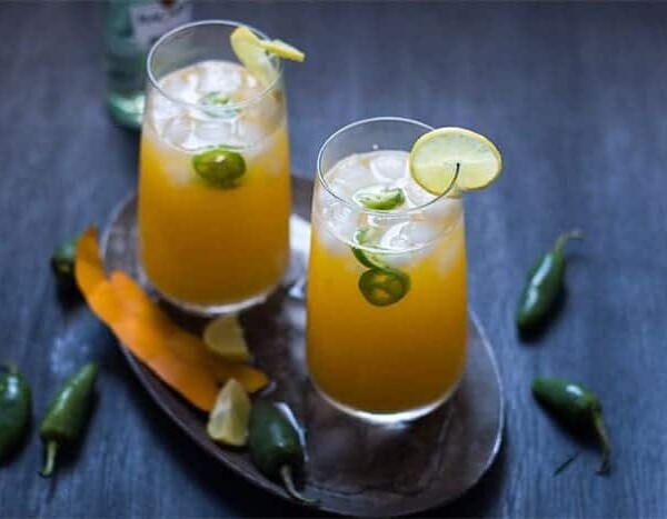Tall Mango Jalapeno Fizzy Cocktail served with ice and a slice of lime in glasses resting on a brown tray.