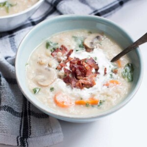 The soup garnished with bacon and cream and served in a white bowl.