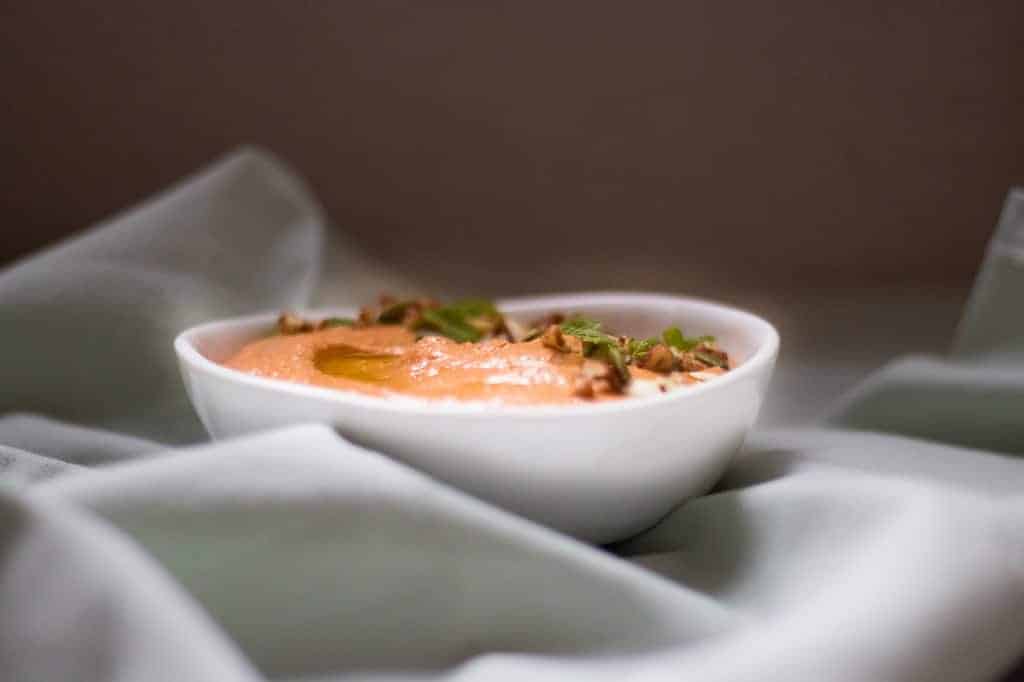 lebanese pecan red pepper dip garnished with pumpkin seeds served in a white bowl