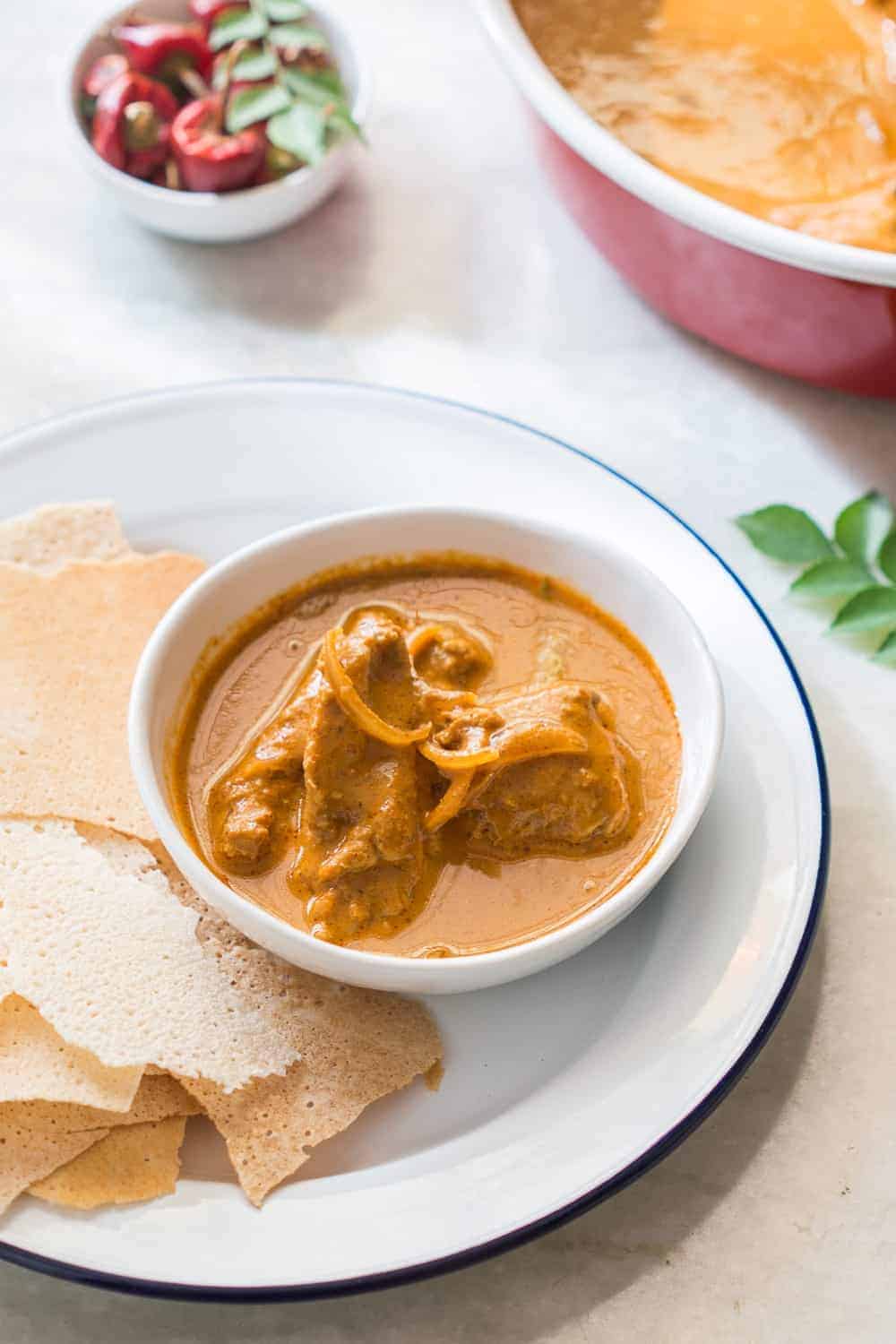 Mangalorean chicken in a white bowl with rotti in a white plate