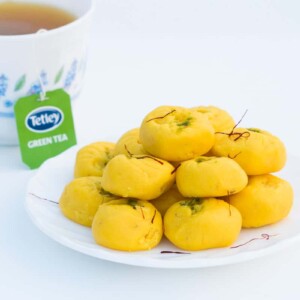 Easy Kesar Pedas served on a white plate with a side of Tetley green tea.