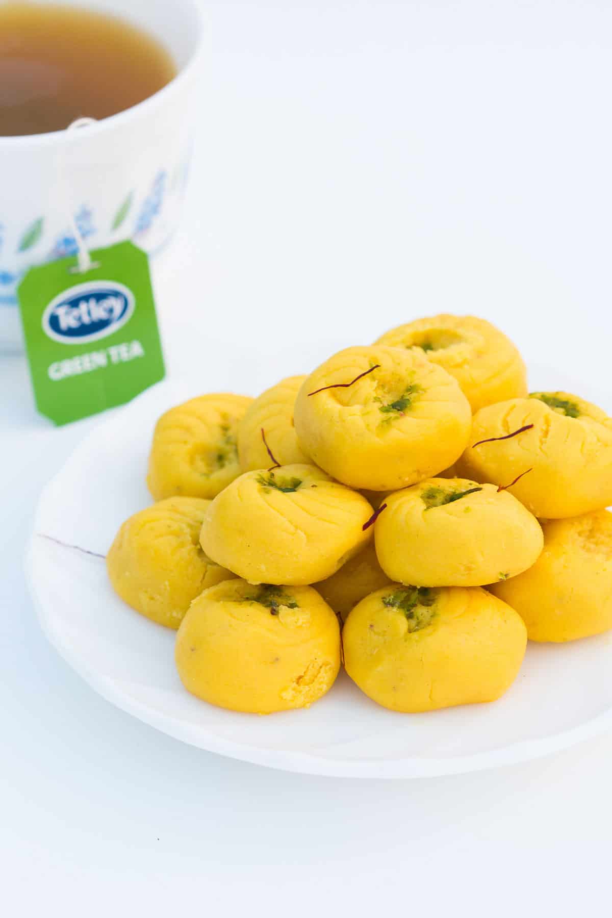 Easy Kesar Pedas served on a white plate with a side of Tetley green tea.