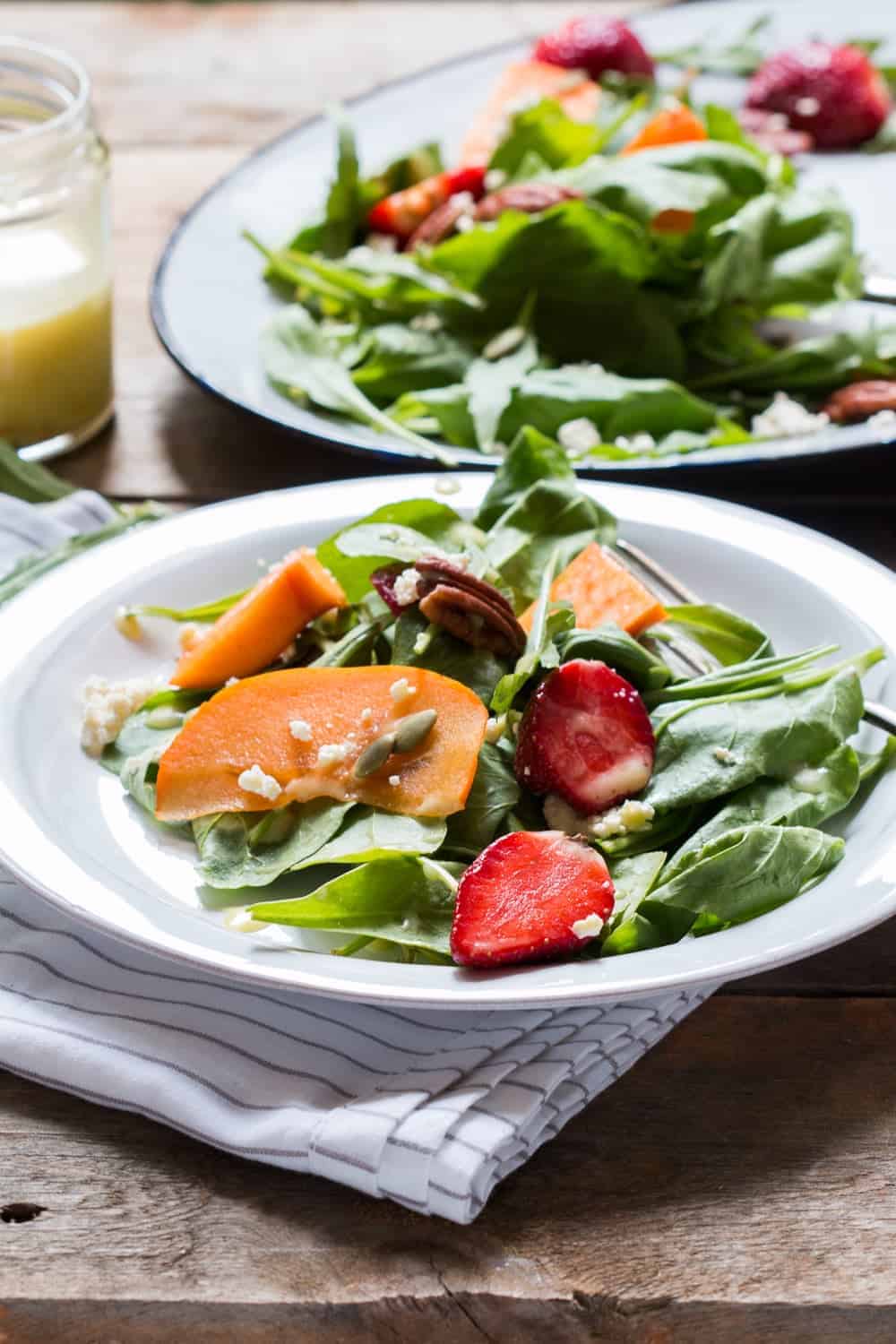 Greens, Persimmon Ricotta Salad with Orange Dressing served in a white plate