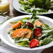 Greens, Persimmon Ricotta Salad with Orange Dressing garnished with ricotta and served in a white plate.