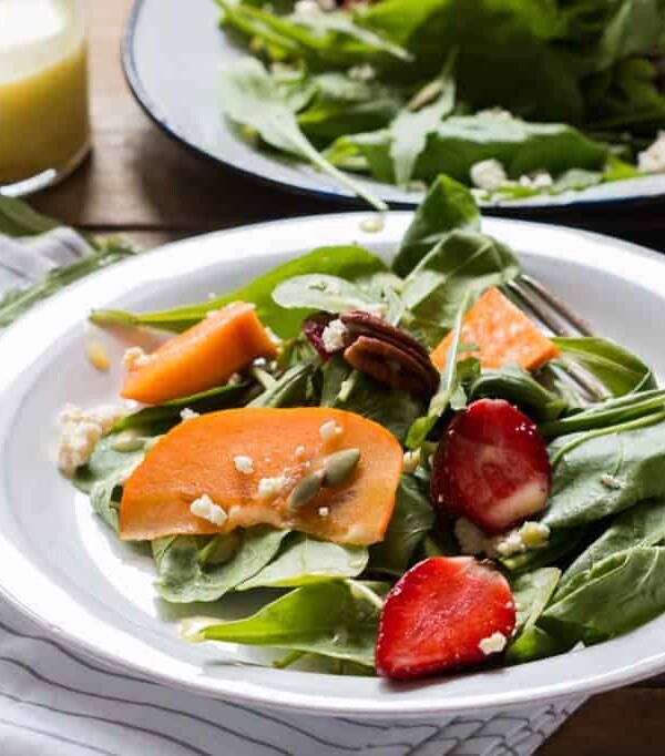 Greens, Persimmon Ricotta Salad with Orange Dressing garnished with ricotta and served in a white plate.