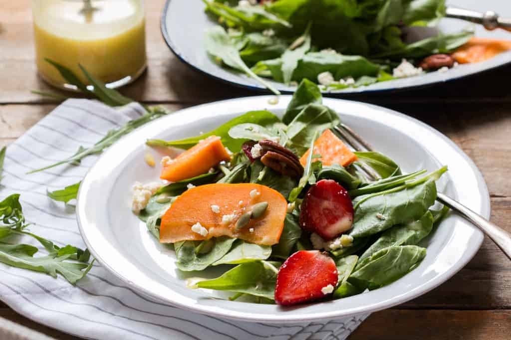 Greens, Persimmon Ricotta Salad with Orange Dressing served in a white plate