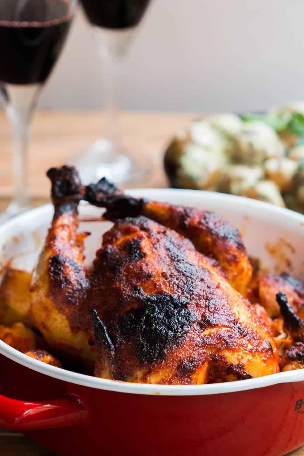 Indian roast chicken served on a bed of onions, potatoes and garlic in a red roasting pan