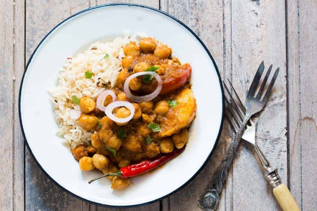 chana aloo masala with rice, cut onions and chilli on a white plate placed a brown board