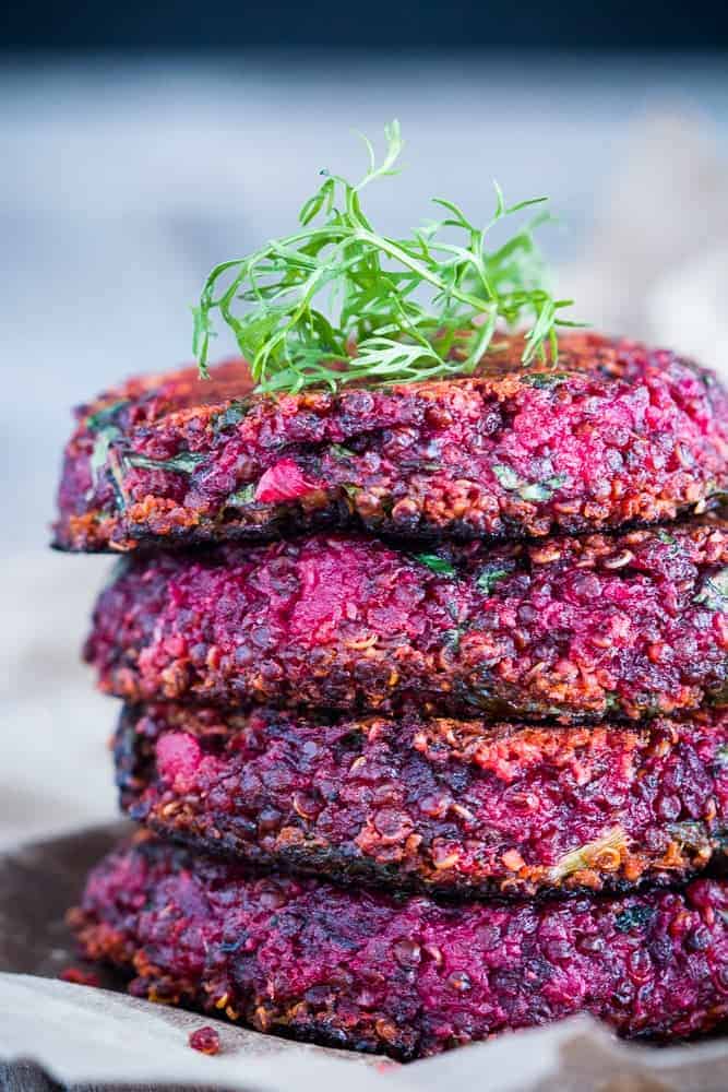Four beet and goat cheese quinoa patties stacked one on top of another placed on crushed white paper