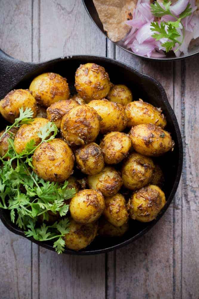 top shot of bombay potatoes with coriander in a cast iron pan with onions, and rotis in a plate on the side