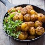 Bombay potatoes garnished with coriander and served in a black pan.