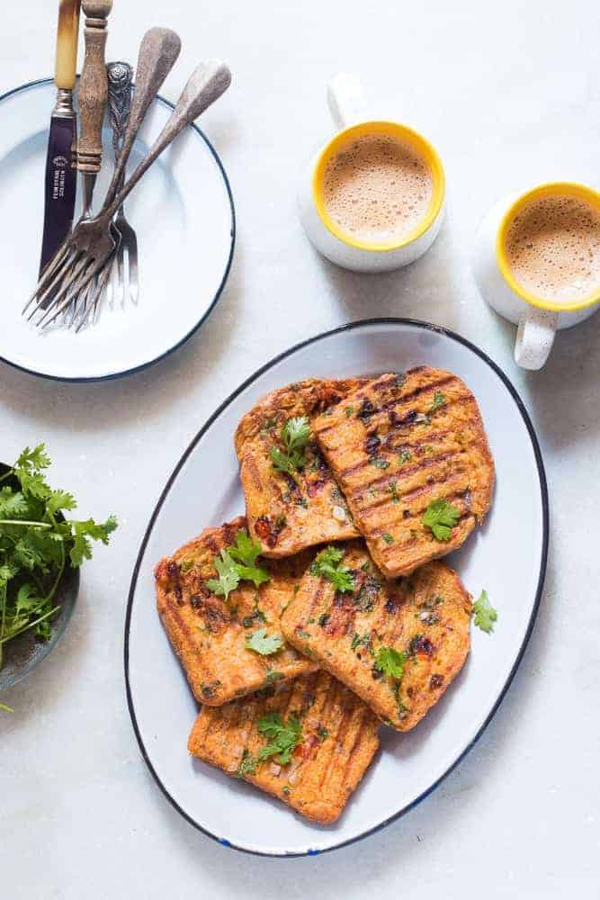 Indian masala egg french toast served in a white plate with hot cups of coffee on the side