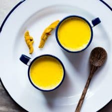 Haldi doodh served in cups kept on a white plate.