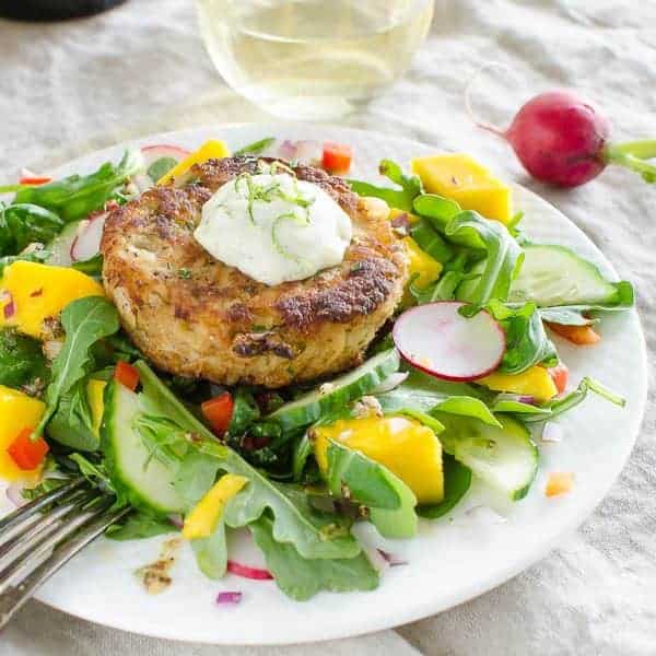 A collection of 13 insanely delicious savoury mango recipes that are sure to blow your mind if you've always had mangoes in sweet dishes. These recipes combine the juicy sweetness of mangoes with savoury ingredients to create a dish that's truly stellar and unforgettable! #spring #mango #recipes #easter #summer #fruit Mango crab cakes with a mango lettuce salad on a white plate with a fork
