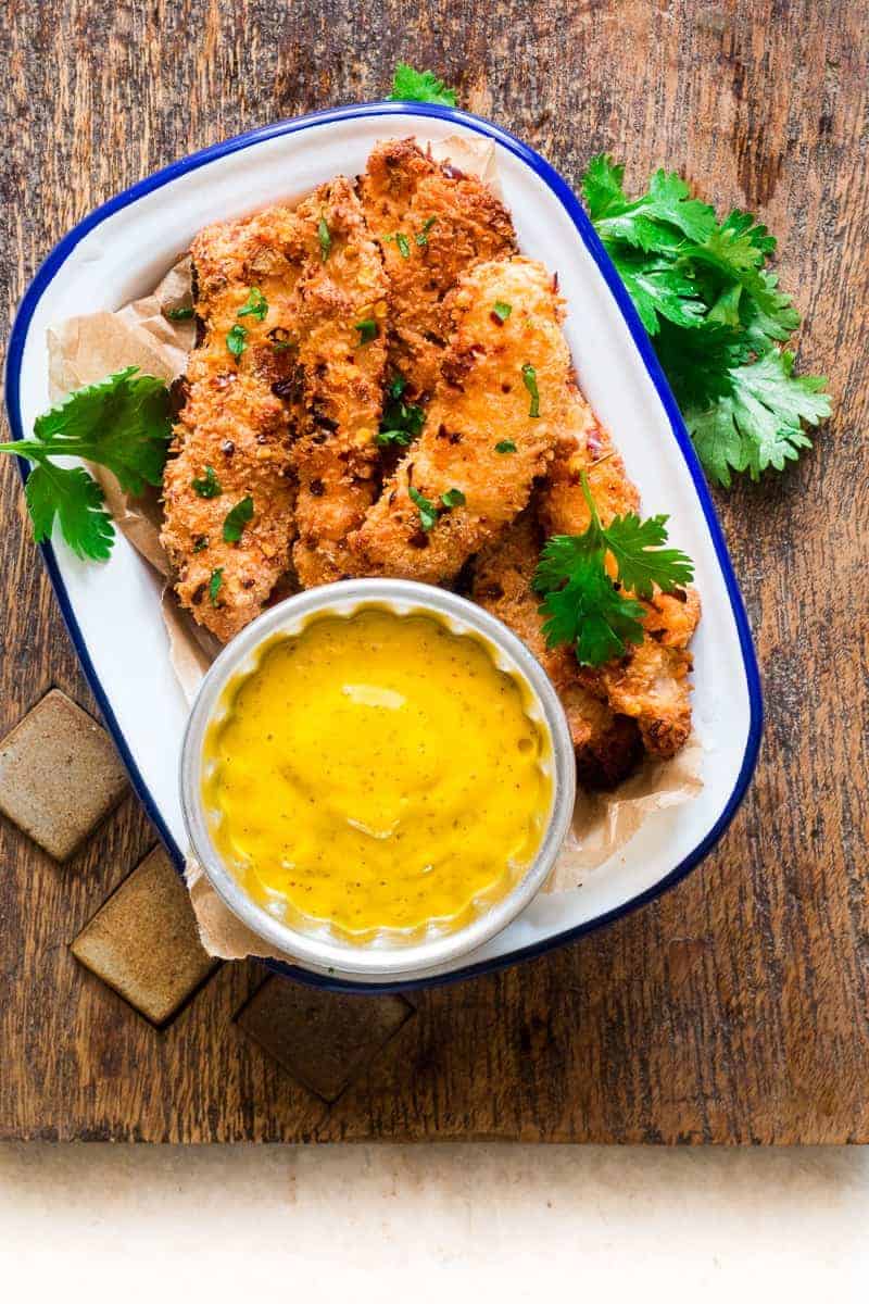 A collection of 13 insanely delicious savoury mango recipes that are sure to blow your mind if you've always had mangoes in sweet dishes. These recipes combine the juicy sweetness of mangoes with savoury ingredients to create a dish that's truly stellar and unforgettable! #spring #mango #recipes #easter #summer #fruit Coconut crusted chicken tenders with a mango dip on a wooden board with cilantro
