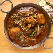 Mutton Curry served in a kadhai with tandoori roti and onions on the side