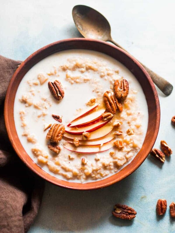 Oatmeal topped with pecans, honey, fresh apple and served in a bowl.