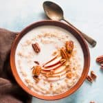 Oatmeal topped with pecans, honey, fresh apple and served in a bowl.