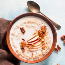 Oatmeal topped with pecans, honey, fresh apple and served in a bowl.