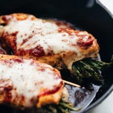 Asparagus Stuffed Chicken Parmesan topped with marinara sauce and prepared in a cast iron pan.