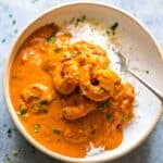 Goan prawn curry ladled over steamed rice and served in a white bowl with a fork on the side