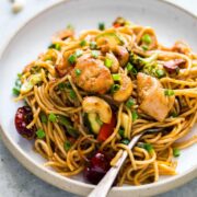 Chinese Cashew Chicken Noodles Stir-Fry garnished with sesame seeds, green onion and served in a white plate.