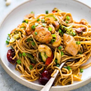 Chinese Cashew Chicken Noodles Stir-Fry garnished with sesame seeds, green onion and served in a white plate.