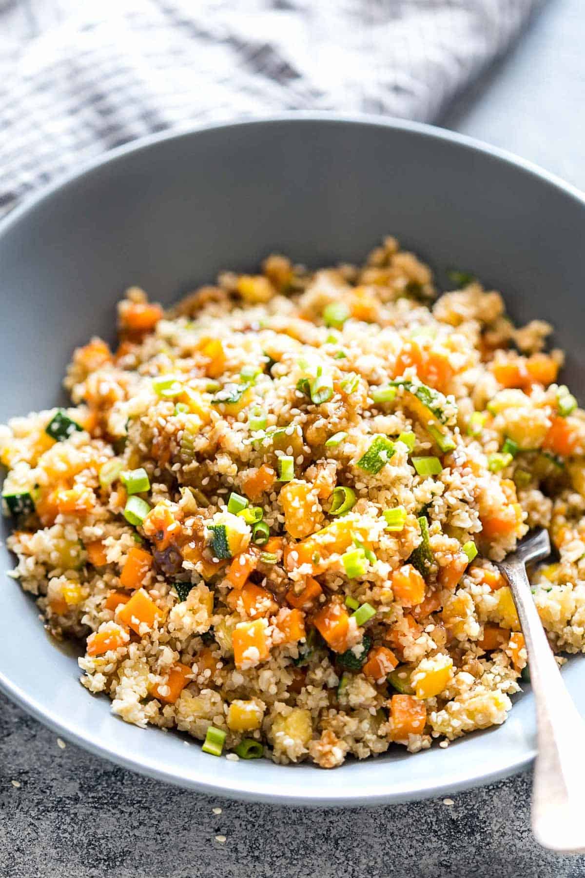 Low Carb Asian Cauliflower Rice topped with sesame seeds, chopped green onions and served in a bowl.