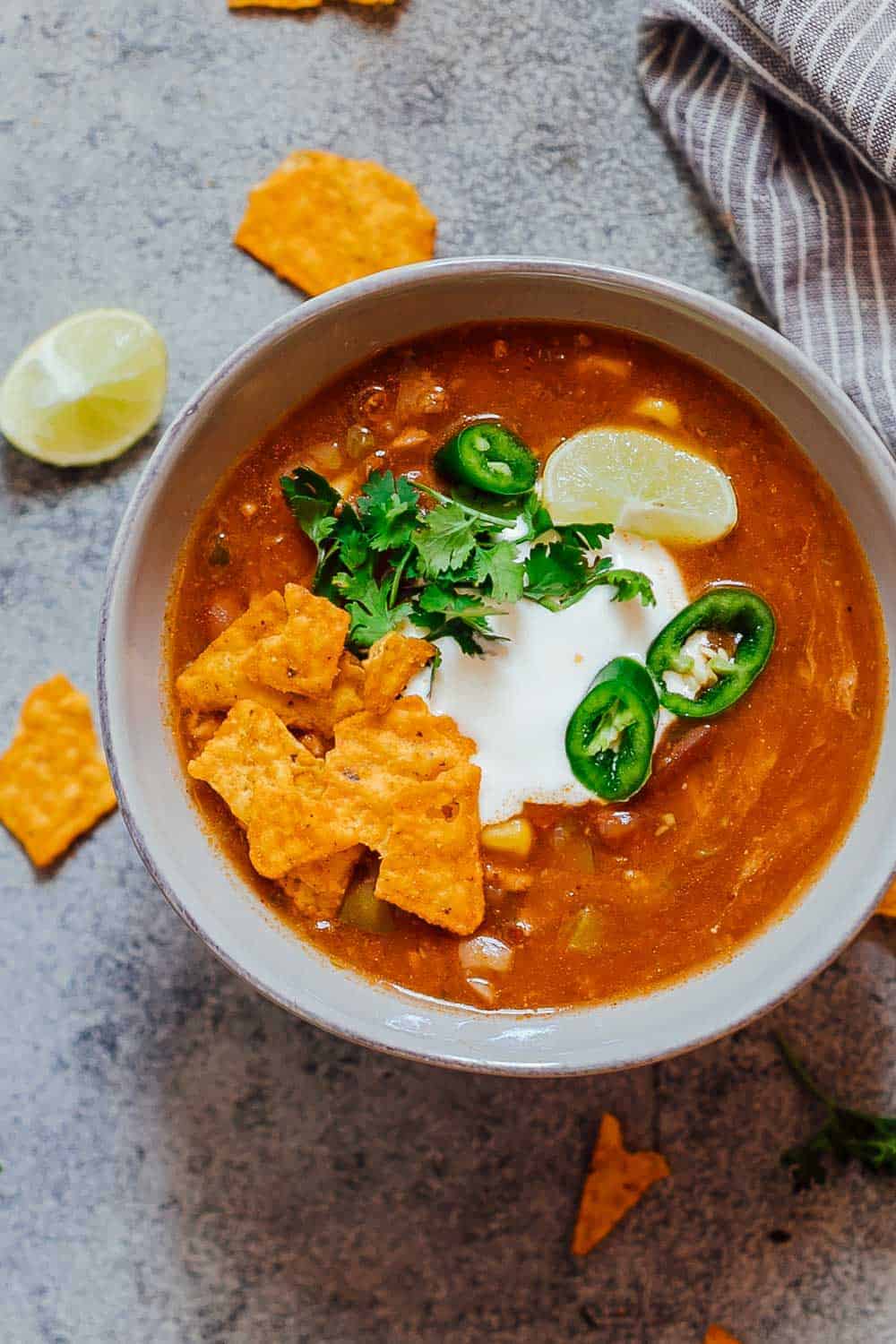 This Chicken Enchilada Soup recipe is like your favourite enchiladas but in soup form. Totally hands off because this is pressure cooked in the Instant Pot and really fast to make. This thick, spicy soup is loaded with beans, corn and chicken and topped with sour cream and cilantro its pure comfort food! Bowl of chicken enchilada soup made in the Instant Pot topped with sour cream, cilantro, sliced jalapenos, tortilla chips and a lime wedge