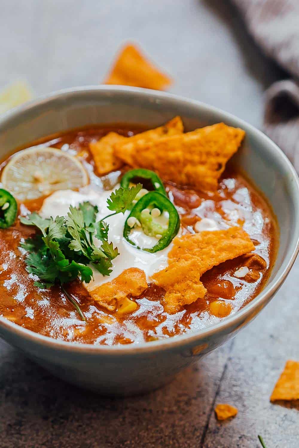 This Chicken Enchilada Soup recipe is like your favourite enchiladas but in soup form. Totally hands off because this is pressure cooked in the Instant Pot and really fast to make. This thick, spicy soup is loaded with bell peppers, beans, corn and chicken and topped with sour cream and cilantro its pure comfort food! Bowl of chicken enchilada soup made in the Instant Pot topped with sour cream, cilantro, sliced jalapenos, tortilla chips and a lime wedge