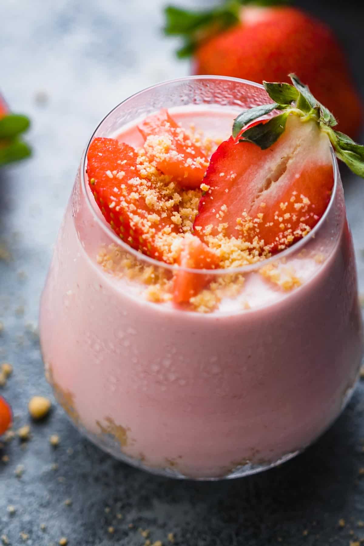 closeup of no bake strawberry cheesecake jars topped with strawberries and biscuit crumb