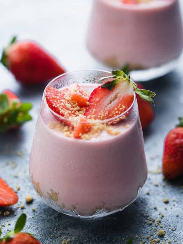 Two No Bake Strawberry Cheesecake Jars with fresh strawberries scattered around