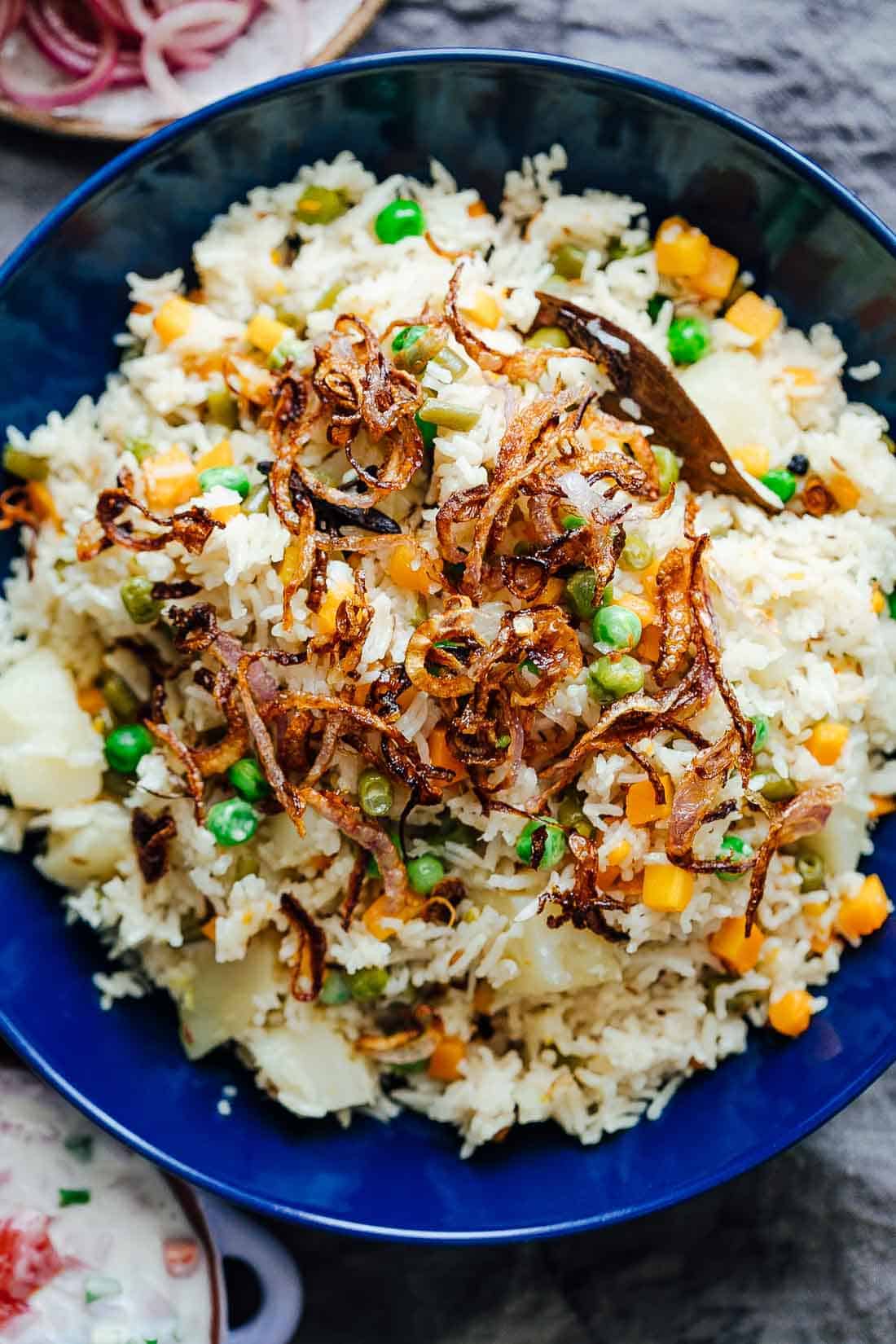 This pressure cooker VEGETABLE PILAF (rice pulao/ pilav) recipe is fragrant, fluffy and perfect every single time! Make this healthy and easy mixed vegetable rice (like biryani) in under 30 minutes. Seasoning includes whole spices and cooked with lots of vegetables, this is the perfect Indian side dish. #sides #recipe #dinner #fast #onepot #vegetarian Pressure cooker veg pulao served in a bowl with crispy onions on top