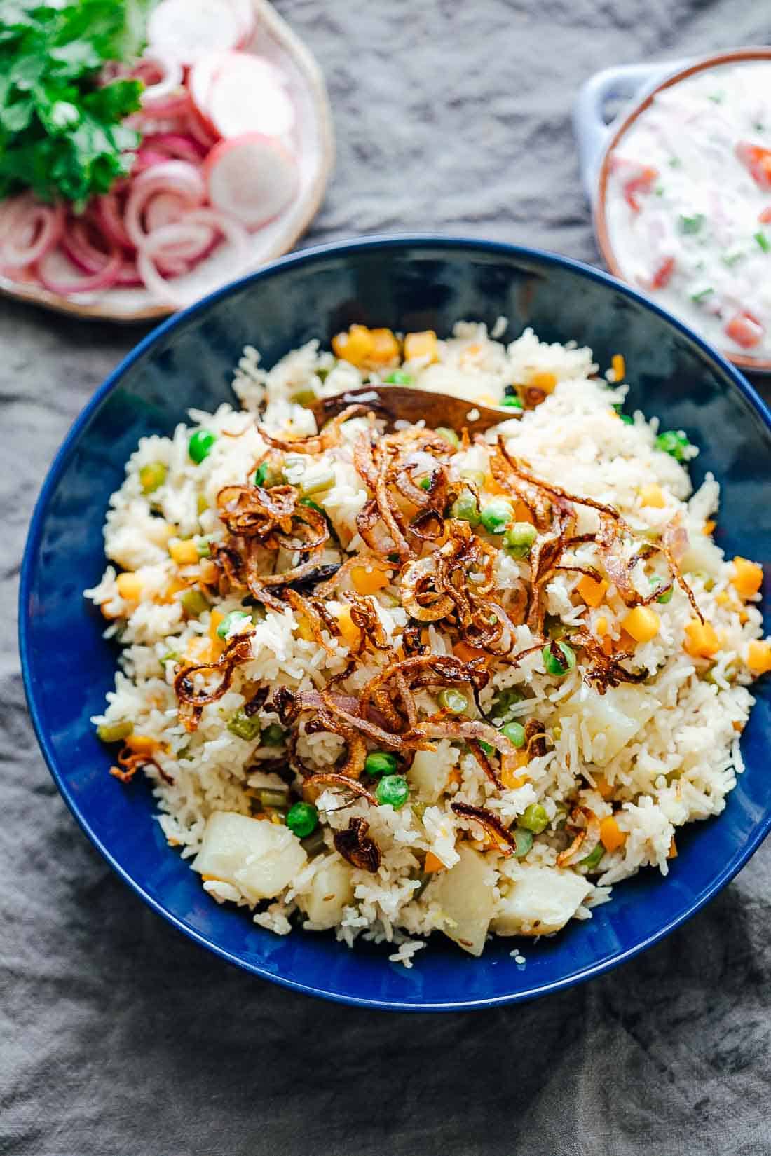 This pressure cooker VEGETABLE PILAF (rice pulao/ pilav) recipe is fragrant, fluffy and perfect every single time! Make this healthy and easy mixed vegetable rice (like biryani) in under 30 minutes. Seasoning includes whole spices and cooked with lots of vegetables, this is the perfect Indian side dish. #sides #recipe #dinner #fast #onepot #vegetarian Pressure cooker veg pulao served in a bowl with crispy onions on top