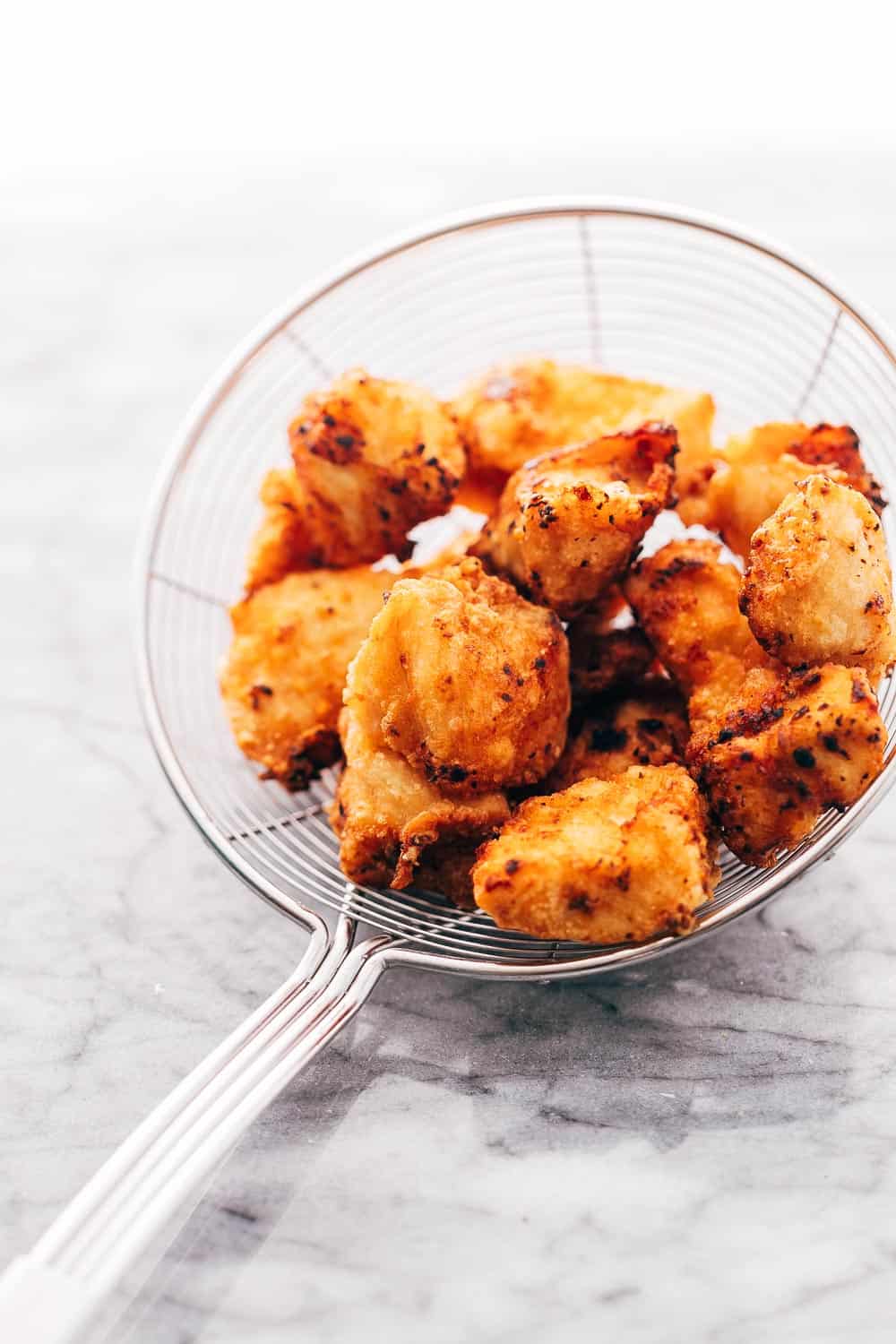 KOREAN POPCORN CHICKEN is sticky, spicy, tangy and crunchy. Inspired by the hyper-famous Korean street snack, Dakgangjeong, boneless chicken is deep fried and tossed in a sweet, sour and spicy sauce that makes every bite super addictive. #chicken #appetizer #party #snack #recipe Fried golden crunchy chicken in a frying sieve