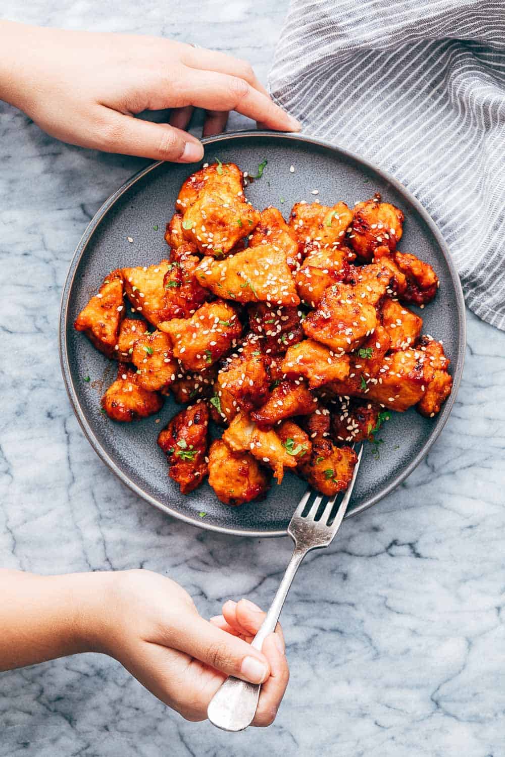 KOREAN POPCORN CHICKEN is sticky, spicy, tangy and crunchy. Inspired by the hyper-famous Korean street snack, Dakgangjeong, boneless chicken is deep fried and tossed in a sweet, sour and spicy sauce that makes every bite super addictive. #chicken #appetizer #party #snack #recipe Korean Popcorn Chicken on a plate with a hand coming up to take a bite with a fork