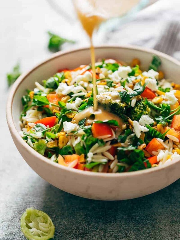 Pouring lemon salad dressing on a bowl of lemon orzo pasta salad to toss it up.