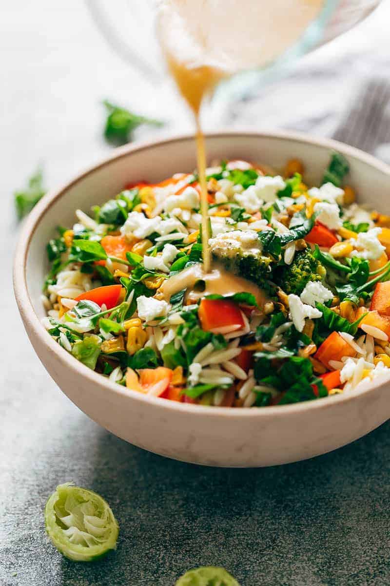 Pouring lemon salad dressing on a bowl of lemon orzo pasta salad to toss it up