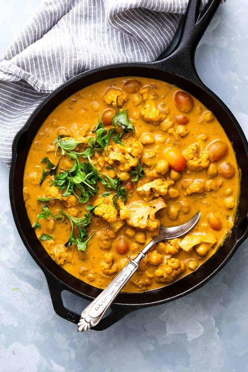 This is a classic coconut curry with tender cauliflower and soft chickpeas thats all made in one pot and has a simple mix of spices. That sauce is super addictive and you'll love how easy it is to make. It's vegan and gluten free, but you can easily add chicken, shrimp, lamb or beef if you prefer meat. #curry #sauce #coconut #cauliflower #dinner Cauliflower Chickpea Coconut Curry straight from the stove to the table in a cast iron skillet with a spoon