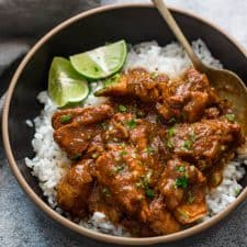 Slow cooker chicken curry served over steamed rice in a black bowl with lemon wedges.