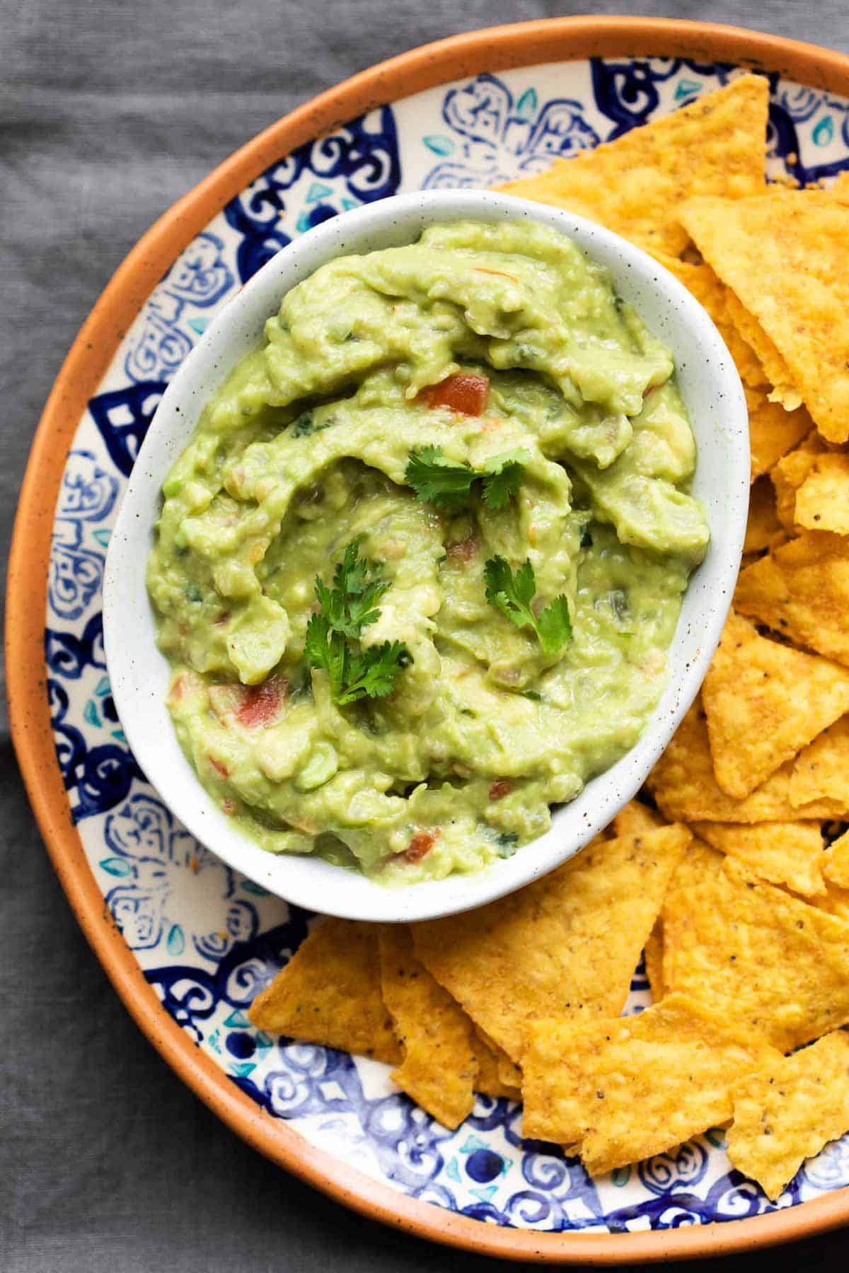 Crazy good homemade guacamole served in a white bowl with chips on the side.
