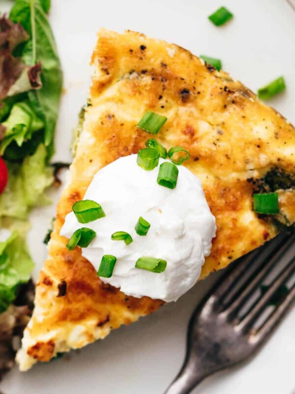 A slice of spinach potato veggie frittata topped with a dollop of sour cream and chopped green onions