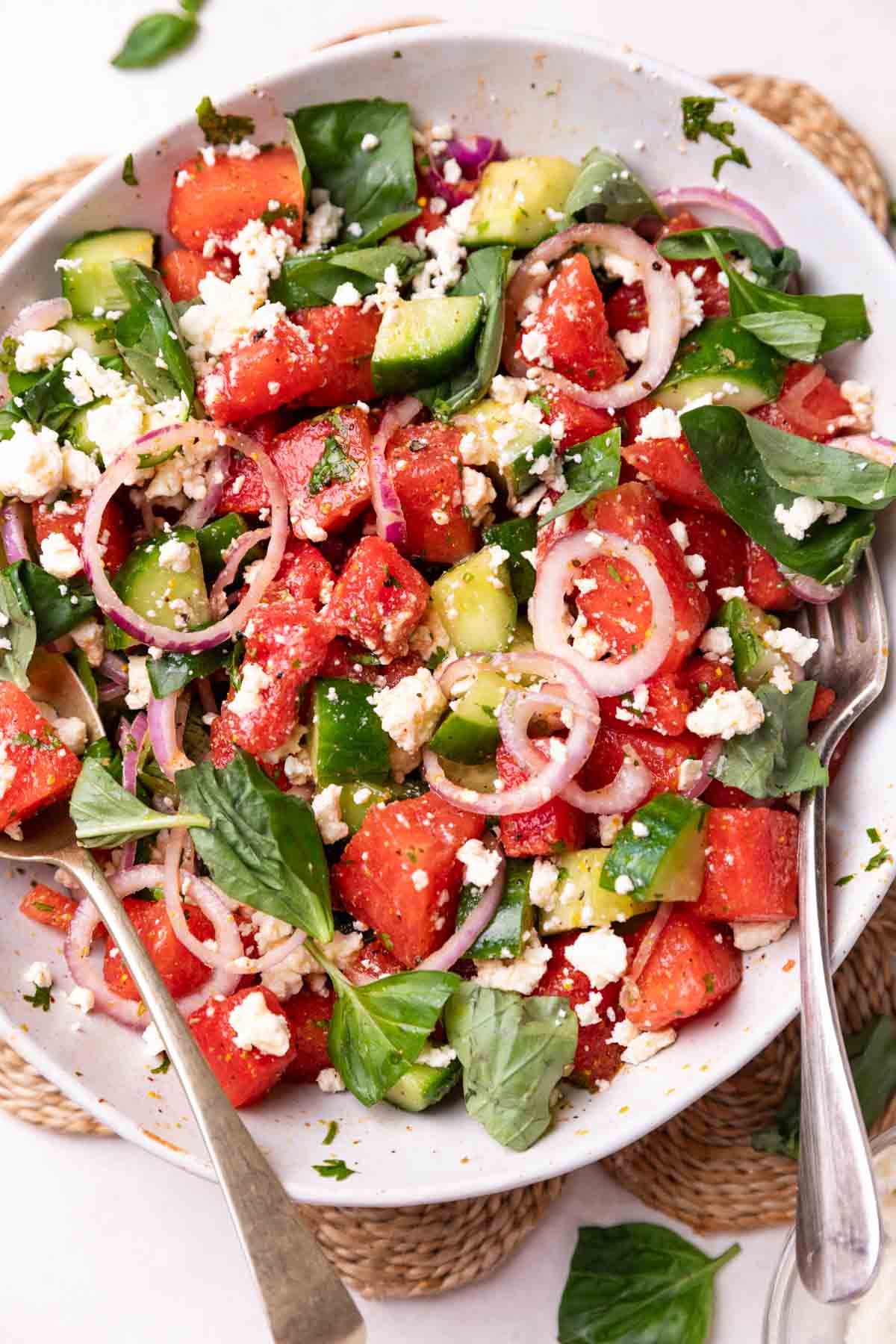 watermelon salad in a white bowl with fork and spoon